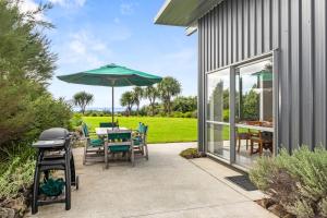 a patio with a table with an umbrella and a grill at Sea View Cottage - Ruakaka Holiday Cottage in Ruakaka