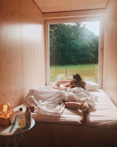 uma mulher deitada numa cama num quarto com uma janela em Slow Cabin - Antwerp em Wuustwezel