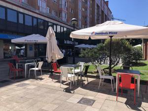 un gruppo di tavoli e sedie con ombrelloni di fronte a un edificio di Urquijo Playa by FlowHome a Gijón