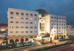 Surabaya Suites Hotel Powered by Archipelago في سورابايا: مبنى ابيض كبير فيه سيارات تقف امامه