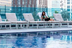 a woman sitting in a chair next to a swimming pool at Unlock Metropolis Business Bay in Dubai