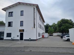 a white building in a parking lot with cars parked at Hotel Pasa Paradies KOSTENLOSE PARKPLÄTZE in Hanau am Main