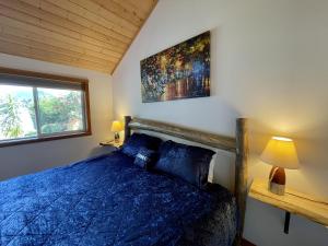 een slaapkamer met een blauw bed en een raam bij Beautiful Oceanfront Cabin With Hot Tub! - Gone With The Wind in Ucluelet