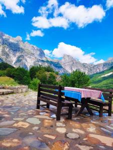 een parkbankje met een tafel erop met bergen op de achtergrond bij Guest House Astrit Villi in Theth