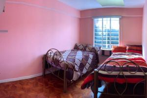 2 camas en una habitación con paredes rosas y ventana en Casa Jardín Recuérdame en Copacabana, en Copacabana