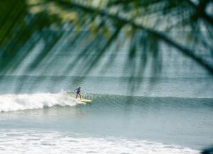 une personne à bord d'une vague sur une planche de surf dans l'océan dans l'établissement Casa Melina Torio Cozy upscale 2bd jungle House, à Torio