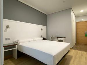 a bedroom with a large white bed and a desk at Hotel Arsus in Vigo