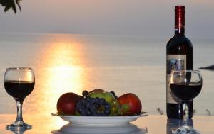 a bottle of wine and a bowl of fruit next to two glasses at Sunset Hotel in Agios Ioannis Kaspaka