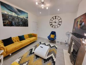 sala de estar con sofá amarillo y reloj en Garland Modern 4 Bedroom Central Apartment London, en Finchley