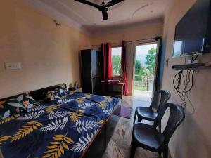 een slaapkamer met een bed en 2 stoelen en een televisie bij Odyssey Stays Rathuadhab (Jim Corbett National Park) in Badīyārgaon