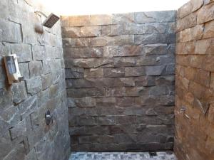 a stone shower in a bathroom with a stone wall at Tiis Garden Puri Villas in Gianyar