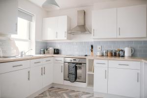 a white kitchen with white cabinets and a sink at Barry Island Beachfront Apartment - Stunning Bay Views and Private Parking in Barry