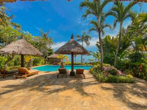 una piscina del resort con sedie, ombrelloni e palme di Villa Bidadari - Bali Sea Villas Beachfront and private pool a Pengastulan