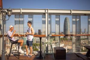 two men sitting at a table on a balcony overlooking a city at Urbany Hostel Barcelona in Barcelona