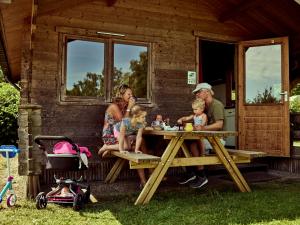 una famiglia seduta a un tavolo da picnic di fronte a una cabina di Trekkershut Plus voor 5 personen incl keuken a Zwiggelte