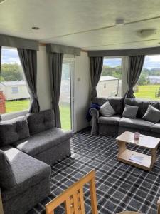 a living room with couches and a table and windows at TL083 - 2 Bedrooms indoor pool Loch Views fishing Golf Riding Shooting Water Sports 15 min drive to beaches PASSES NOT INCLUDED Most Activities Will Not Be Available Out Of Season Please Check Before Booking in Newton Stewart