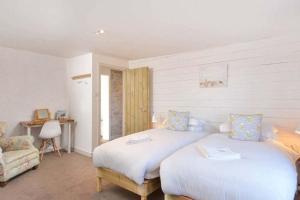 a white bedroom with two beds and a chair at Mick's Cottage in Crail