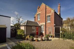 a brick house with a red door and some potted plants at Heywood Cottage in St. Andrews