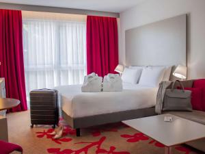 トゥールにあるメルキュール トゥール ノールの大きなベッドと赤いカーテンが備わるホテルルームです。