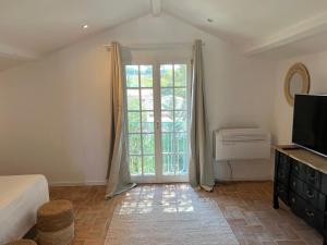 a bedroom with a bed and a tv and a window at Maison d'Orange - La Pinede in Saint-Tropez