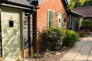 uma casa de tijolos com uma porta verde e janelas em The Foxes Den em Assington