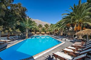 una piscina con tumbonas y palmeras en un complejo en Meltemi Village Hotel en Perissa