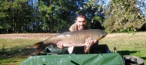 Een man met een grote vis in een zak. bij L’Etang Carp fishing lake and Gite in Saint-Junien