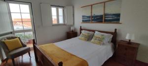 um quarto com uma cama, uma cadeira e uma janela em Casa com Cor na Zambujeira do Mar