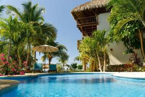 a swimming pool with an umbrella and palm trees at Hotel Bajito Bay in Troncones