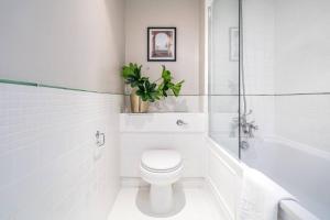 a white bathroom with a toilet and a tub and a plant at Be London - Marylebone Residences in London