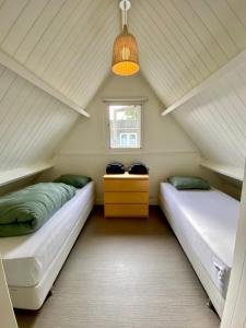 two beds in a attic bedroom with a window at Heerlijk vrijstaand huis aan de duinen in Burgh Haamstede