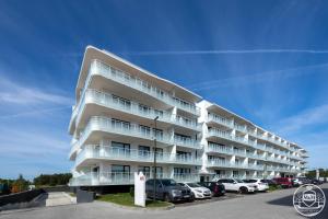 a white apartment building with cars parked in a parking lot at Polanki Aqua - Aquapark, Free Parking, Apartments M&M Kołobrzeg in Kołobrzeg