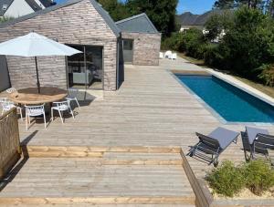 eine Terrasse mit einem Tisch und einem Sonnenschirm neben einem Pool in der Unterkunft Magnifique villa avec piscine, à 5 min des plages in Landunvez