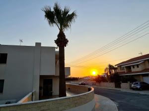 a palm tree in front of a building with the sunset at PylaApts - Apartments near the beach in Pyla