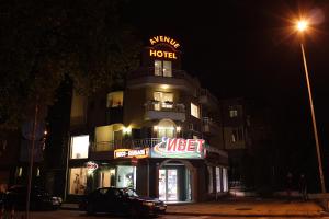 a hotel with a sign on top of it at night at Avenue in Shumen