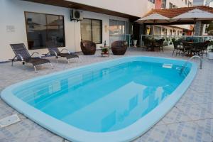 a large blue swimming pool with chairs and tables at Hotel Suiça Faber in Balneário Camboriú