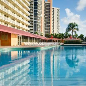 a large swimming pool with chairs and a building at Ramada Marco Polo Beach in Miami Beach