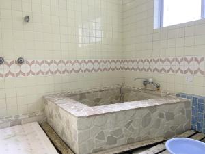 a large tub in a bathroom with a tile wall at Yoshioka Ryokan in Kamogawa