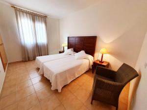 a bedroom with a large white bed and a chair at Apartamentos Las Dunas-B in Riumar