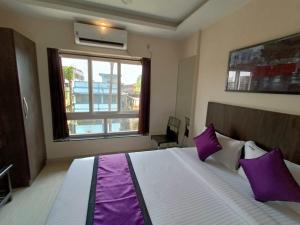 a bedroom with a bed with purple pillows and a window at Sheldon Inn Kolkata in Kolkata