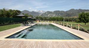 a swimming pool with a wooden deck and mountains in the background at Olimagio Farm Stay with animals and 25m pool, beach at cycling distance in Pietrasanta