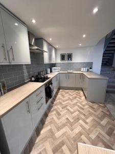 a kitchen with white cabinets and a wooden floor at Stay at The Penn! 5 Bedroomed home in Treharris in Treharris