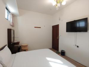 a bedroom with a white bed and a flat screen tv at JINGTONGYULI BnB in Yuli