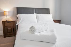 een wit bed met een opgerolde handdoek erop bij Weatherhead Lodge - Modern and Sleek Derby Apartment in Derby