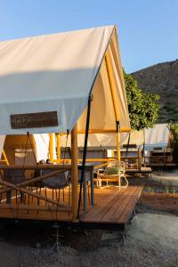wecamp Cabo de Gata في لاس نيغراس: خيمة صفراء وبيضاء تجلس على سطح خشبي