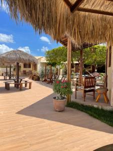 eine Terrasse mit Tischen, Stühlen und einem Strohschirm in der Unterkunft Pousada Rio Aratuá in Galinhos