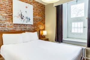 a bedroom with a white bed and a brick wall at Hotel Ermitage in Quebec City