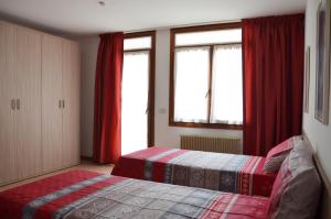 ピエーヴェ・ディ・カドーレにあるAppartamento Giada Pozzale di Pieve di Cadore(BL)のベッドルーム1室(ベッド2台、赤いカーテン付きの窓付)