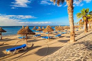 uma praia com guarda-sóis e cadeiras de palha e o oceano em Luminoso y bonito apartamento con piscina en frente del mar em Los Cristianos