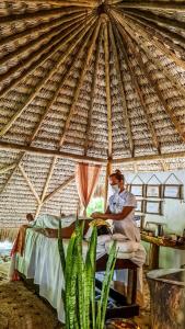 uma mulher sentada numa tenda de palha com uma planta em Casa das Rendas em Praia de Moitas